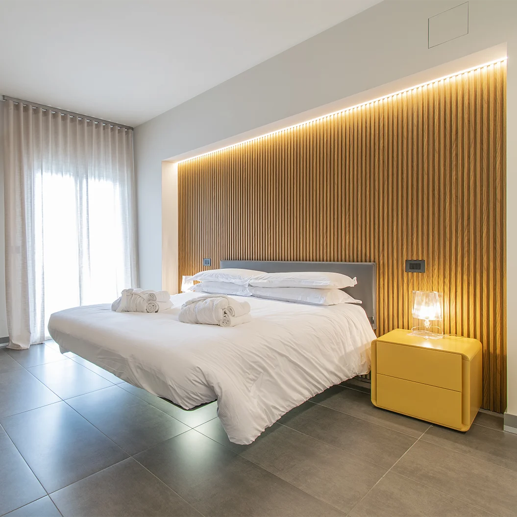 Letto sospeso con comodino giallo e boiserie retroilluminata