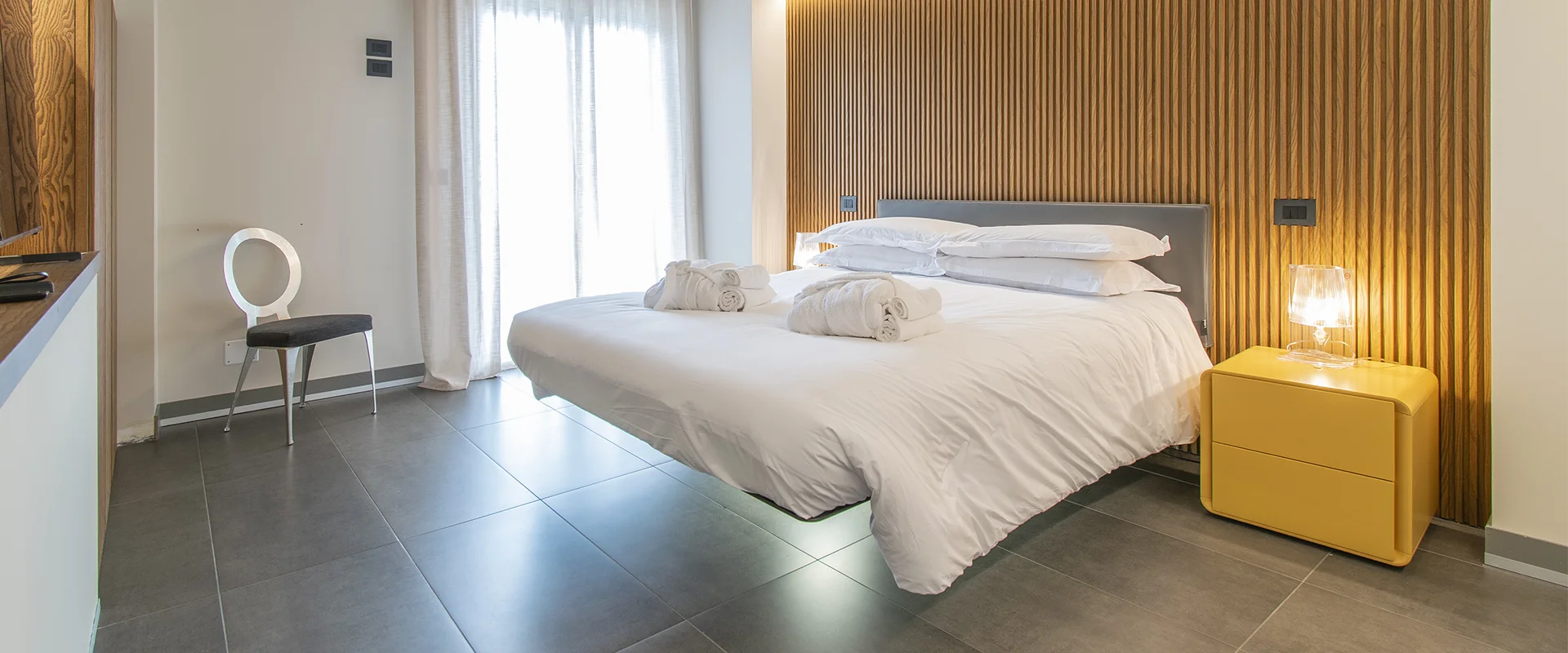Camera con letto sospeso, boiserie in legno e comodino giallo